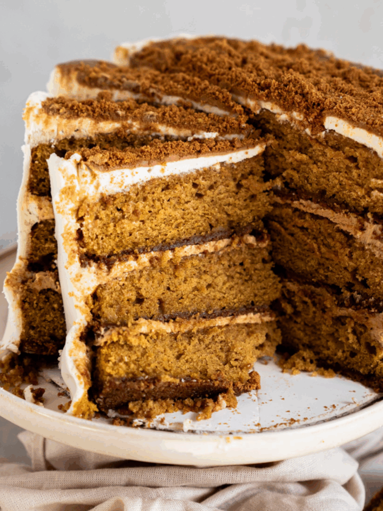 Slice of pumpkin biscoff cake showing biscoff cookie crust and pumpkin spice cake layers