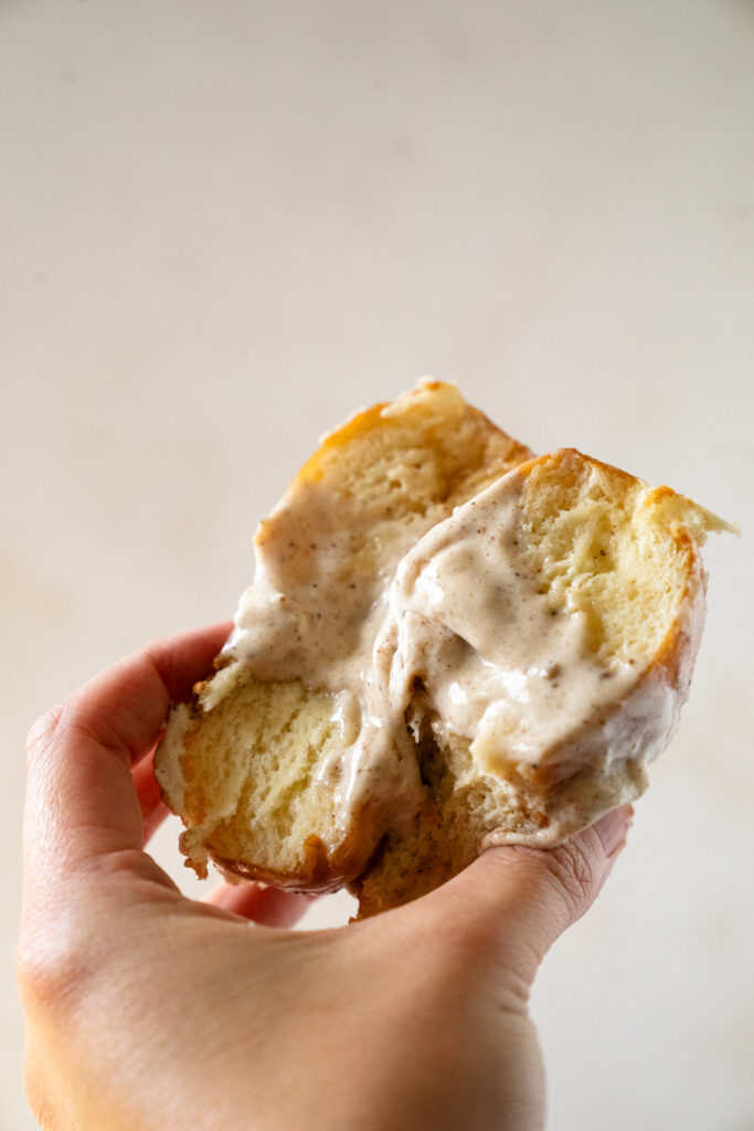 Dipping fluffy donuts into sweet chai glaze in a small bowl